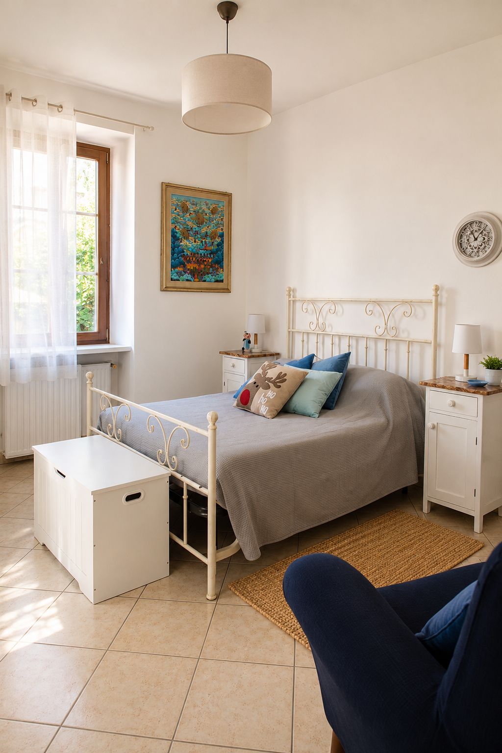 Camera matrimoniale luminosa della Stanza Blu di Casa della Torre, con letto in ferro battuto bianco, comodini e poltrona.