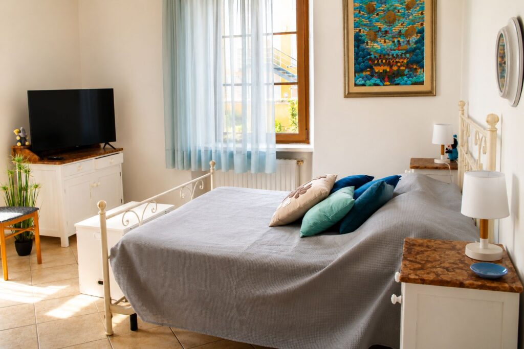 Letto matrimoniale della Stanza Blu di Casa della Torre, con testiera in ferro battuto bianco e cuscini blu.