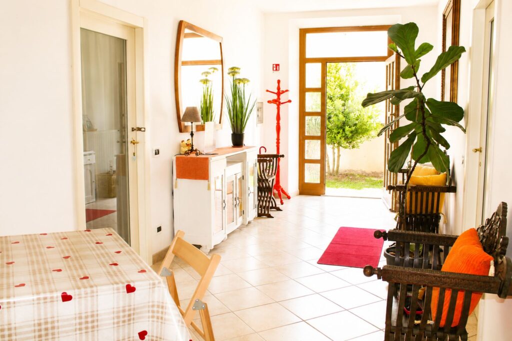 Corridoio luminoso di Casa della Torre con tavolo da pranzo, poltrone in legno e porta sul giardino.