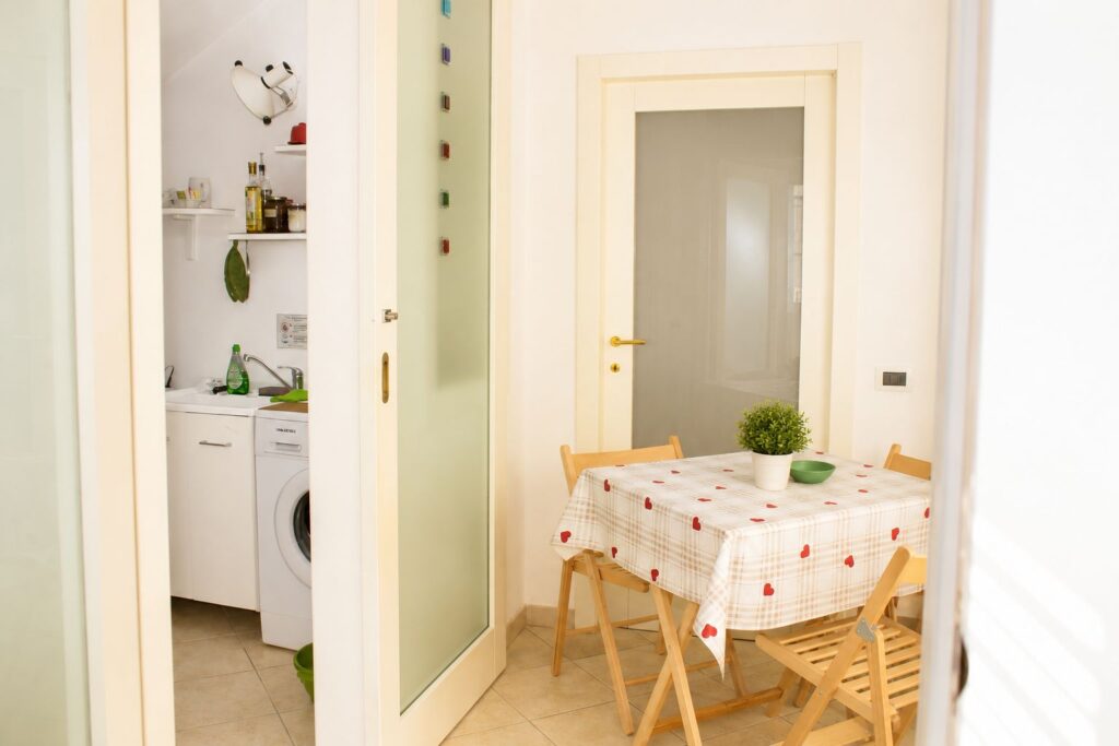 Zona pranzo di Casa della Torre con tavolo, sedie in legno e accesso al cucinotto e al bagno.
