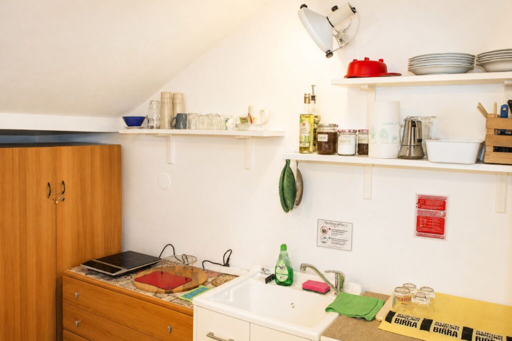Cucina attrezzata della foresteria con piano cottura, lavello, stoviglie e utensili.