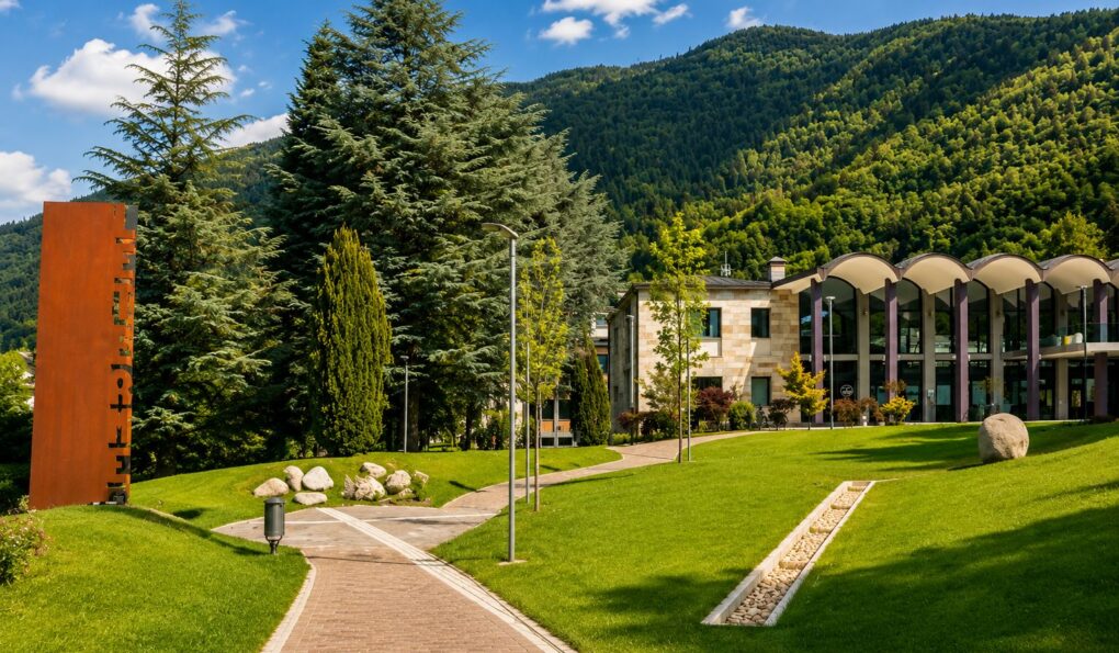 Parco delle Terme di Levico immerso nel verde, con edificio termale e montagne del Trentino sullo sfondo.