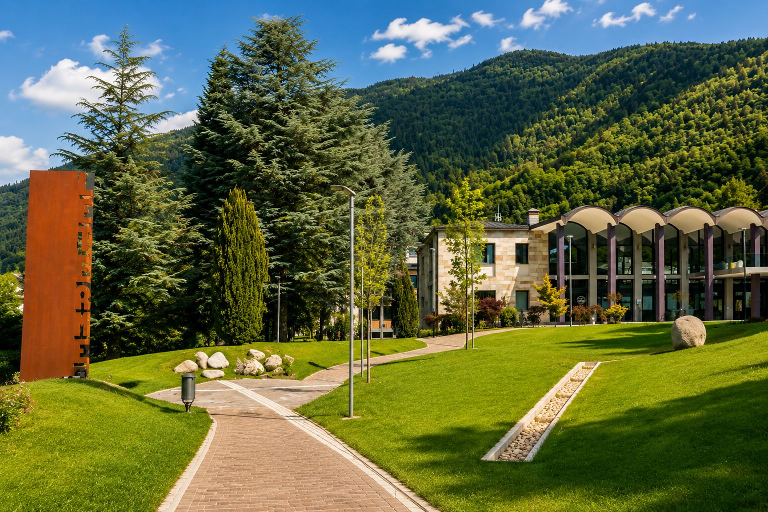 Parco delle Terme di Levico immerso nel verde, con edificio termale e montagne del Trentino sullo sfondo.